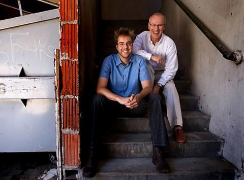 Color photograph of Dries Buytaert and Jay Batson, co-founders of Acquia, sit on external steps smiling