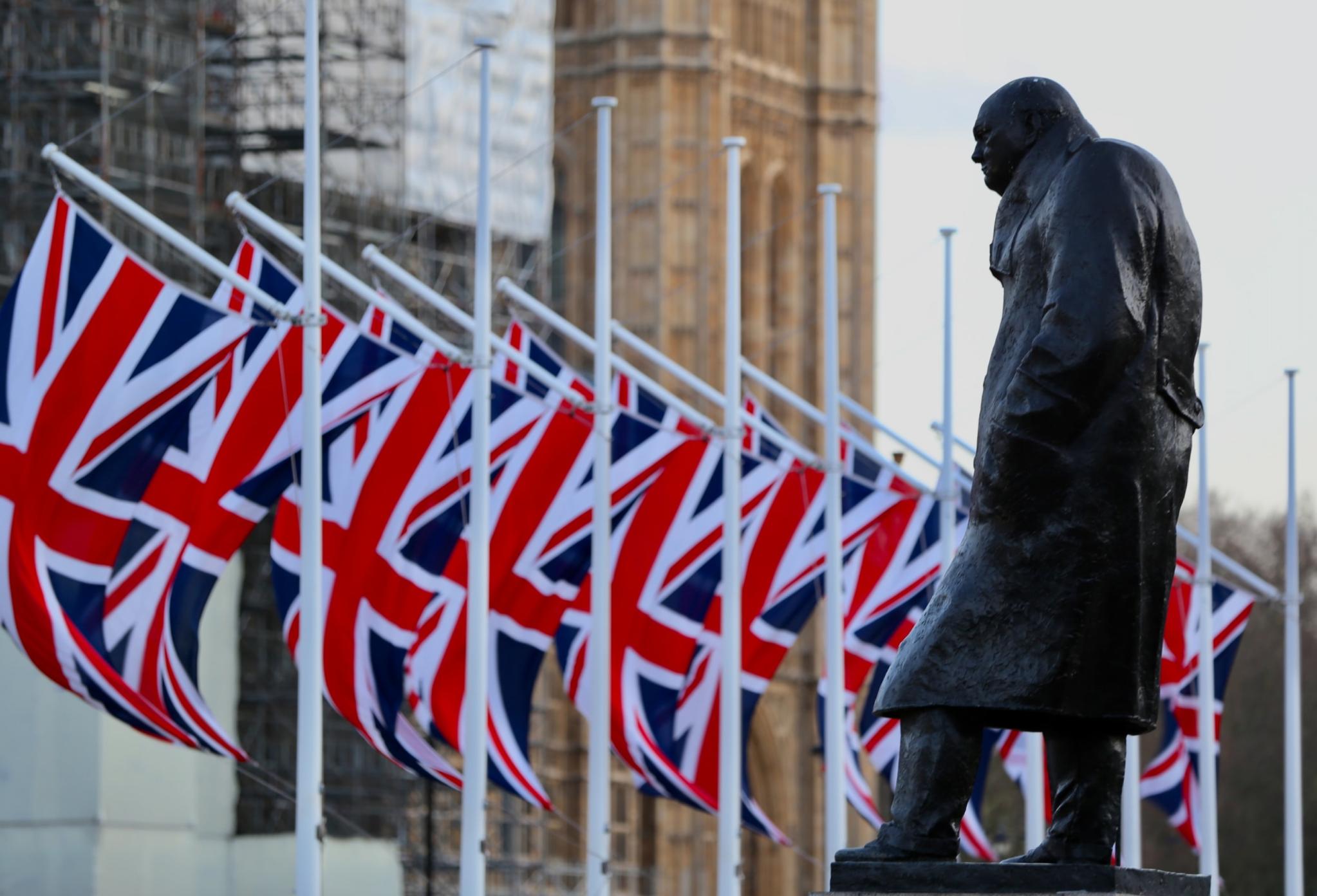 a Series of UK flags with a statue of a political figure in front