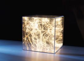 Color photo of transparent cube filled with a jumbled mass of lit strings of light