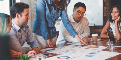 Meeting with five individuals reviewing printed out charts