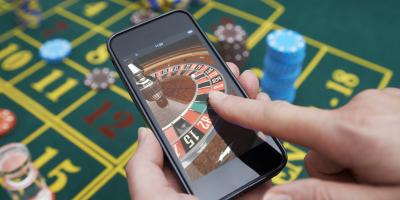 Casino table with hand holding smartphone with roulette on screen