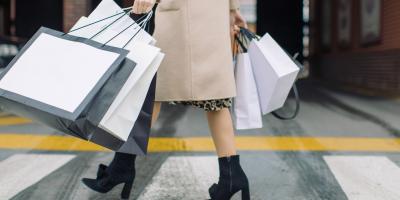 Bottom half of female consumer carrying shopping bags across a crosswalk