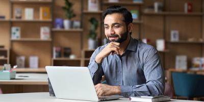 Man sits at a desk, looking at a laptop screen