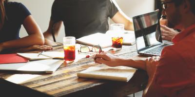 Four people sit around a table with laptops, books, and drinks.