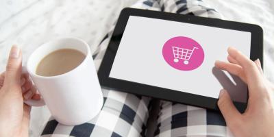 Person holding coffee cup in left hand and device with a shopping cart icon in right hand