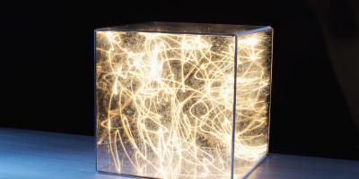 Color photo of transparent cube filled with a jumbled mass of lit strings of light