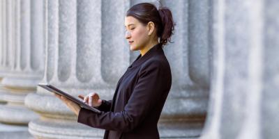 Color photo of woman standing with digital tablet in front of massive columns
