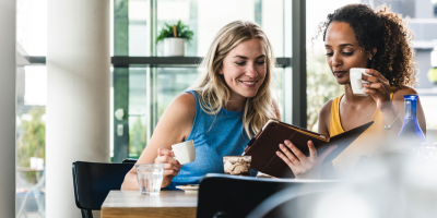 Two women drinking coffee and reading on a shared tablet