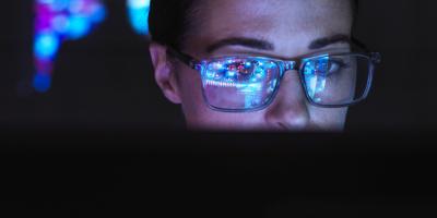 Woman wearing glasses looking at computer screen reflected on her lenses