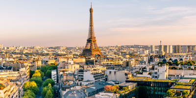 Eiffel Tower rises above Paris cityscape at sunset with tree-lined avenue and urban buildings.