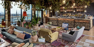 Spacious living room with exposed wooden beams, colorful seating areas, and large windows overlooking water.