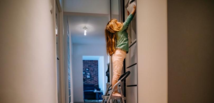 Child on step stool reaching for storage bin on high shelf