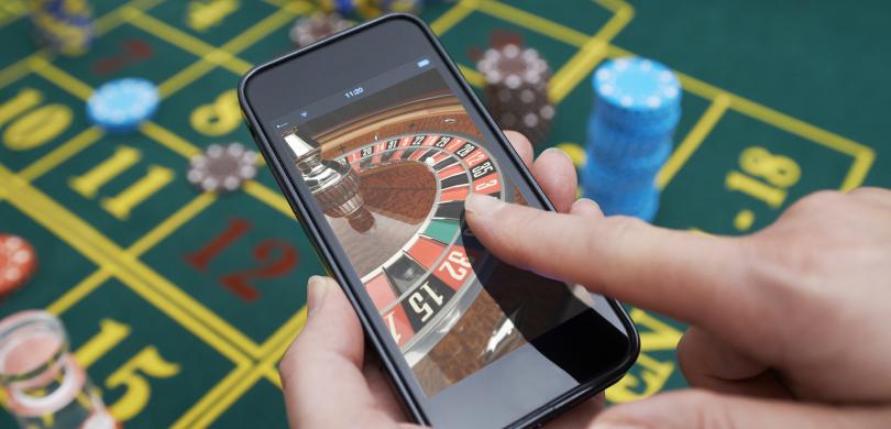 Casino table with hand holding smartphone with roulette on screen