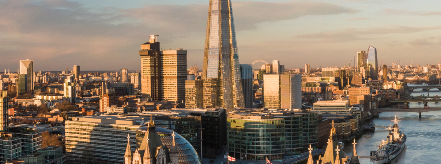 London skyline at sunset featuring Tower Bridge and The Shard skyscraper over the Thames River.