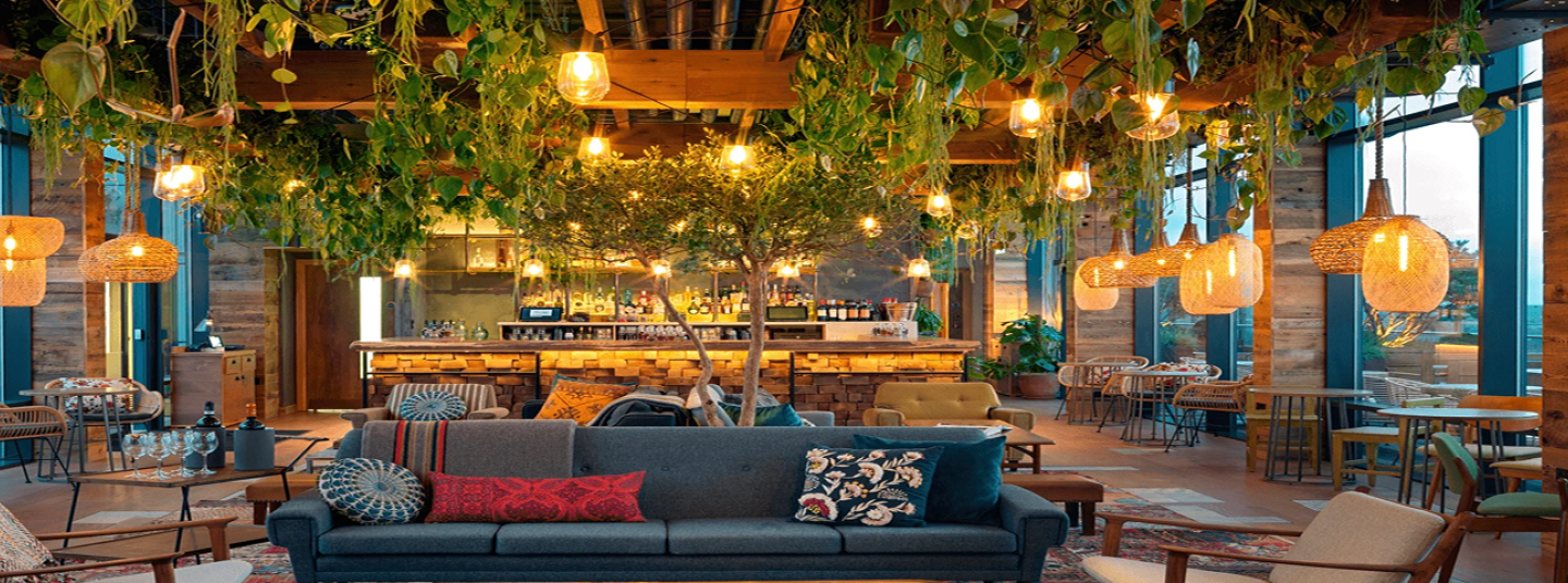 Modern living room with dark sectional sofa, exposed brick walls, hanging plants, and warm ambient lighting.