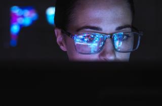 Woman wearing glasses looking at computer screen reflected on her lenses