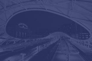 Dark blue-tinted view of curved subway tunnel with train tracks and platform lighting