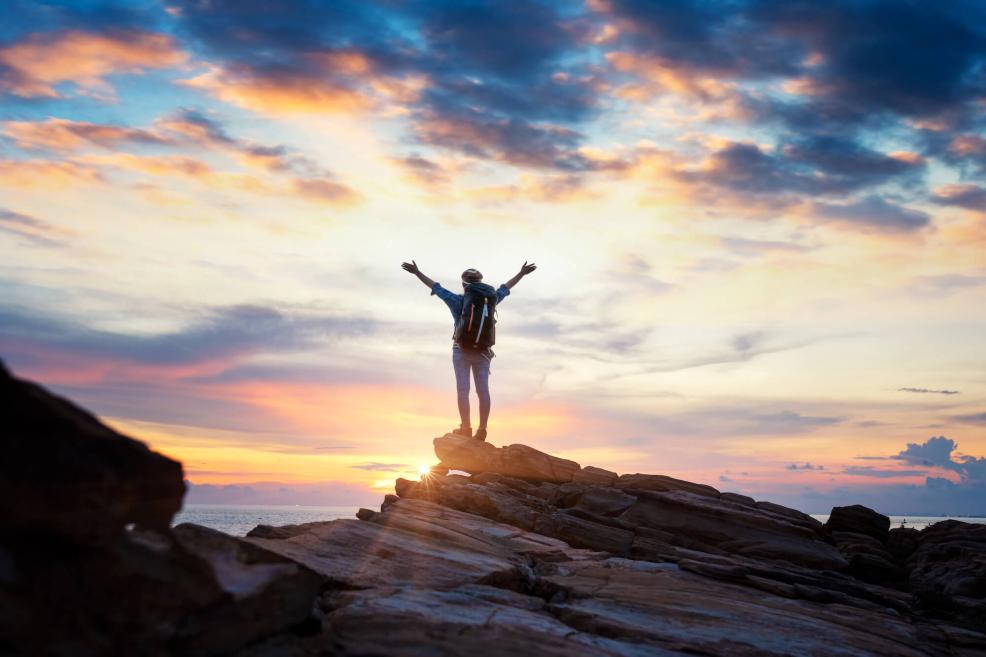 Person standing on summit with arms up in sky during sunrise