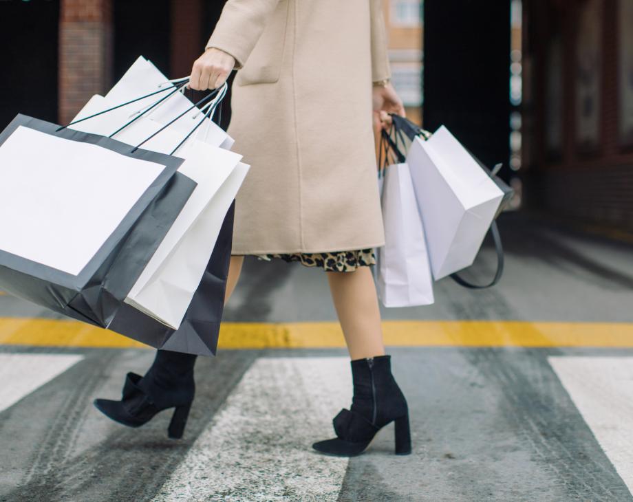Bottom half of female consumer carrying shopping bags across a crosswalk