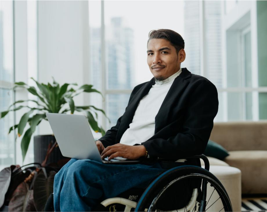 Color photo of Hispanic man in a wheelchair and holding a laptop
