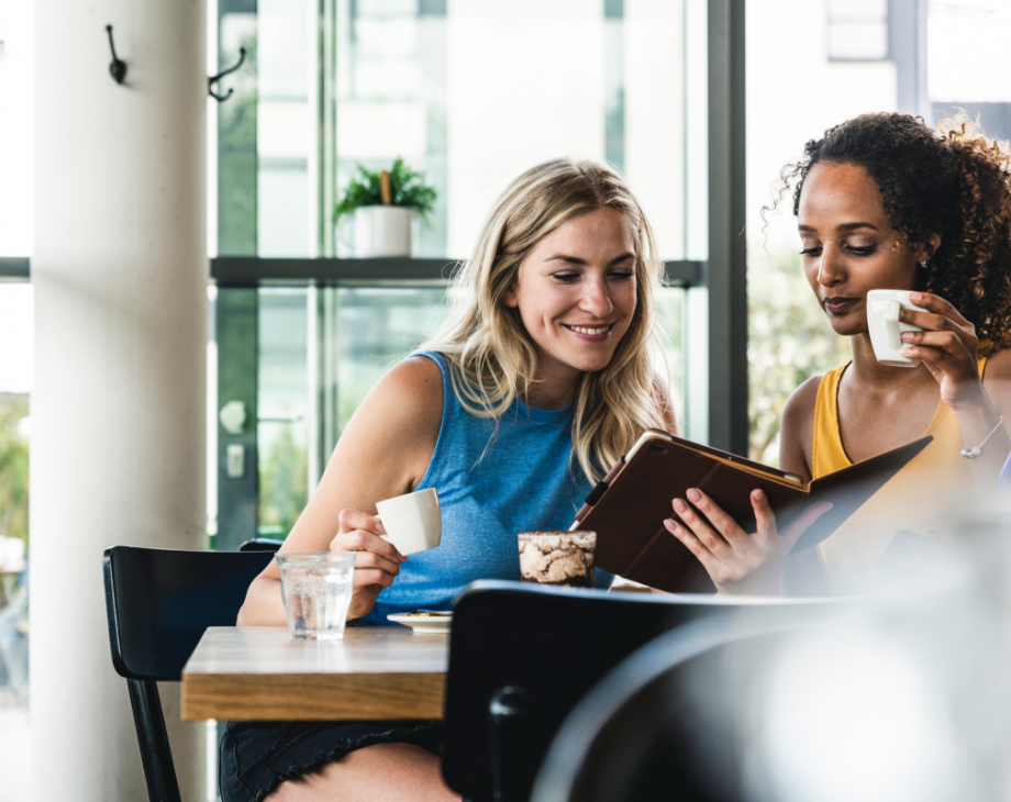Two women drinking coffee and reading on a shared tablet