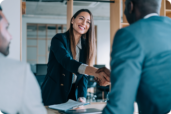 Two businesswomen shaking hands across a desk during a professional meeting