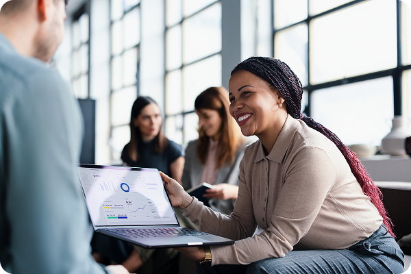 Woman in headset smiling while working on laptop in modern office with colleagues