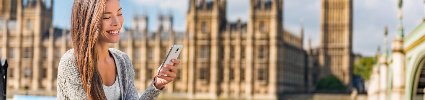 Woman sitting across river from Parliament and Big Ben using smartphone