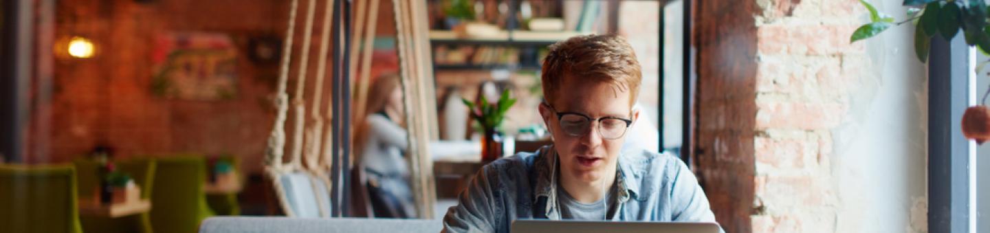 Man in glasses sitting alone at cafe table with laptop