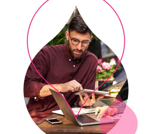 Man in burgundy shirt writing at desk with laptop and plant